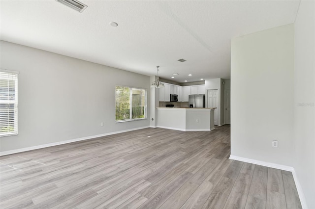 unfurnished living room featuring light hardwood / wood-style flooring, a notable chandelier, and a textured ceiling