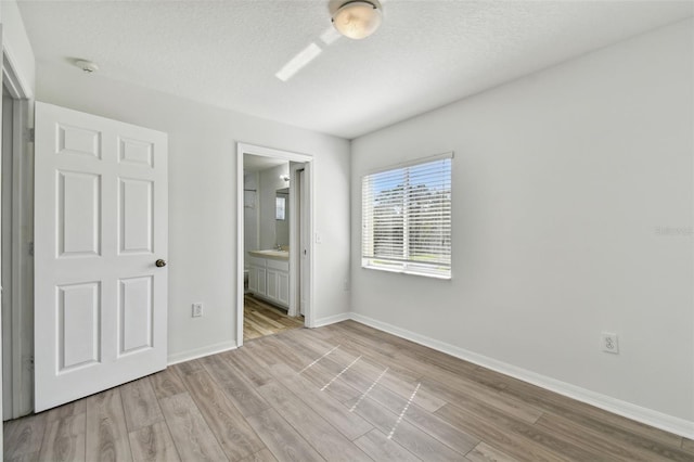 unfurnished bedroom with connected bathroom, light hardwood / wood-style flooring, and a textured ceiling