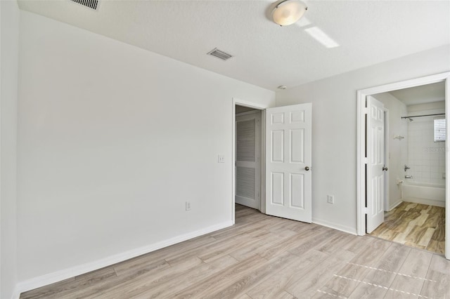 unfurnished bedroom with connected bathroom, a textured ceiling, and light hardwood / wood-style flooring