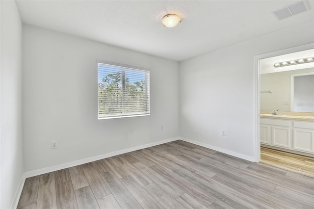 unfurnished bedroom featuring connected bathroom, sink, and light hardwood / wood-style floors