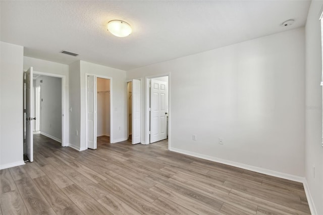 unfurnished bedroom featuring a closet, a textured ceiling, a spacious closet, and light wood-type flooring