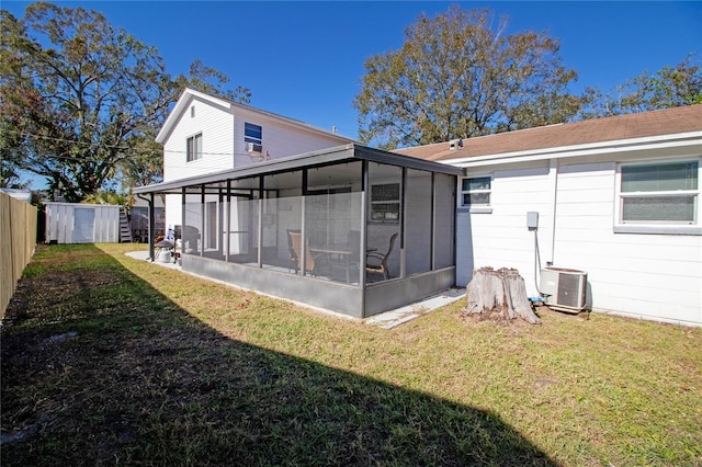 rear view of house featuring central air condition unit, a sunroom, a yard, and a storage unit