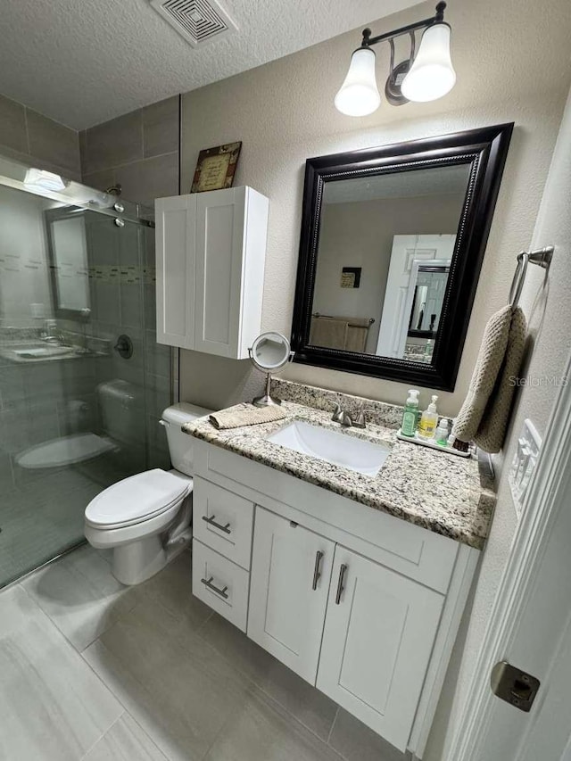 bathroom with vanity, a textured ceiling, a shower with door, tile patterned flooring, and toilet