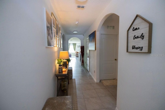 hall with a textured ceiling and light tile patterned floors