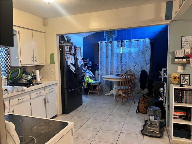 kitchen with tasteful backsplash, light tile patterned floors, electric range, white cabinets, and black fridge