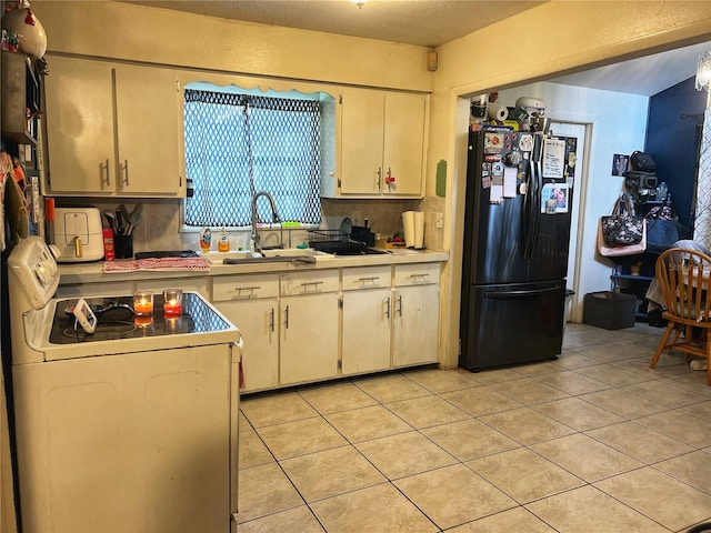 kitchen with white range oven, sink, light tile patterned flooring, black fridge, and decorative backsplash