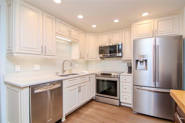 kitchen with white cabinets, appliances with stainless steel finishes, sink, and light hardwood / wood-style flooring