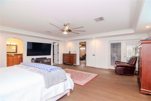 bedroom with a raised ceiling, hardwood / wood-style floors, ensuite bath, ornamental molding, and ceiling fan