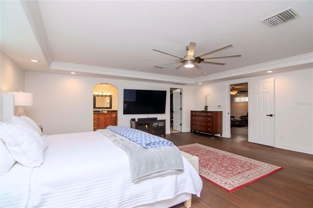 bedroom with dark hardwood / wood-style floors, a tray ceiling, ensuite bath, ornamental molding, and ceiling fan