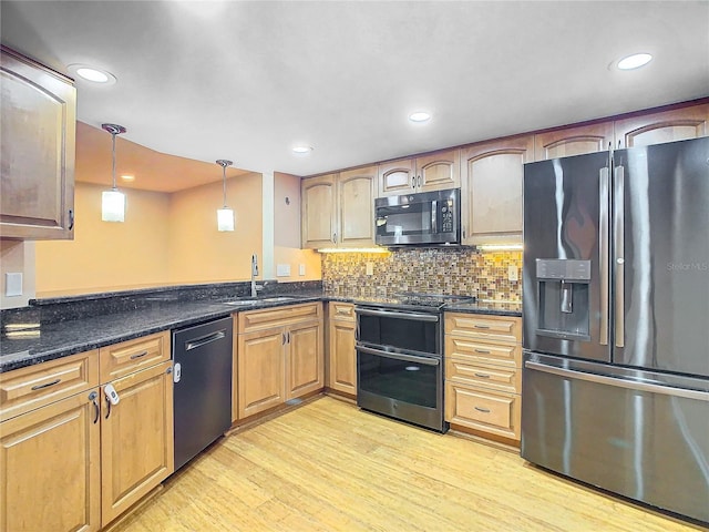 kitchen featuring hanging light fixtures, appliances with stainless steel finishes, light wood-type flooring, dark stone countertops, and sink