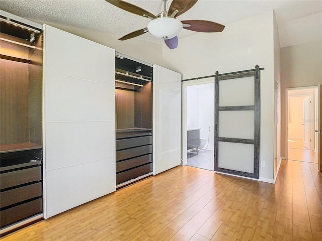 unfurnished bedroom featuring ensuite bathroom, wood-type flooring, a barn door, a textured ceiling, and ceiling fan