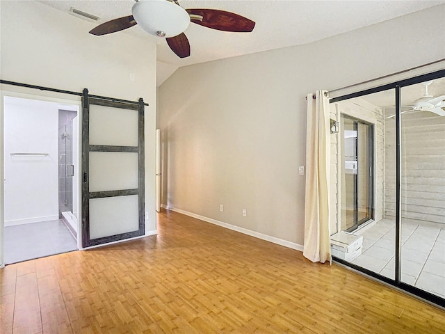 empty room featuring a barn door, a textured ceiling, ceiling fan, lofted ceiling, and light hardwood / wood-style flooring