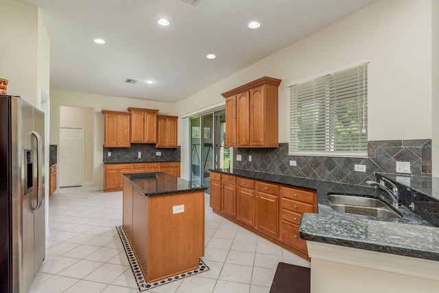 kitchen with stainless steel fridge, sink, backsplash, a center island, and dark stone countertops