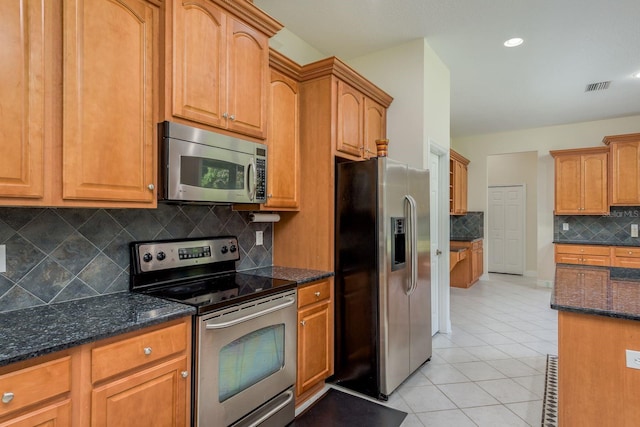 kitchen featuring dark stone counters, backsplash, appliances with stainless steel finishes, and light tile patterned floors