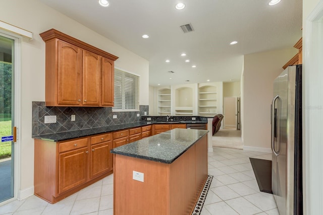 kitchen with dark stone countertops, stainless steel fridge, light tile patterned floors, and a center island