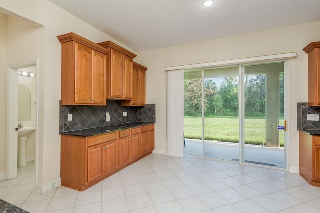 kitchen with sink, light tile patterned floors, tasteful backsplash, a textured ceiling, and dark stone counters