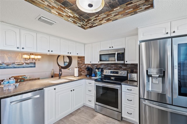 kitchen with stainless steel appliances, sink, tasteful backsplash, dark stone countertops, and white cabinets