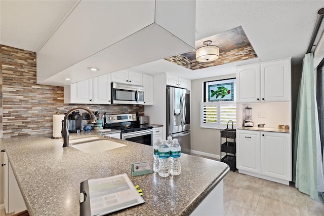 kitchen with backsplash, appliances with stainless steel finishes, sink, white cabinets, and a tray ceiling