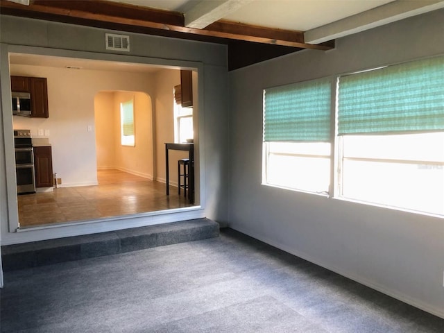 carpeted spare room featuring beamed ceiling