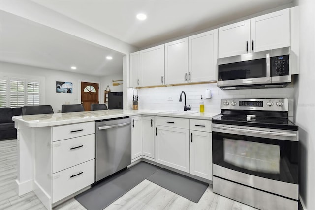 kitchen with white cabinetry, kitchen peninsula, stainless steel appliances, hardwood / wood-style flooring, and sink