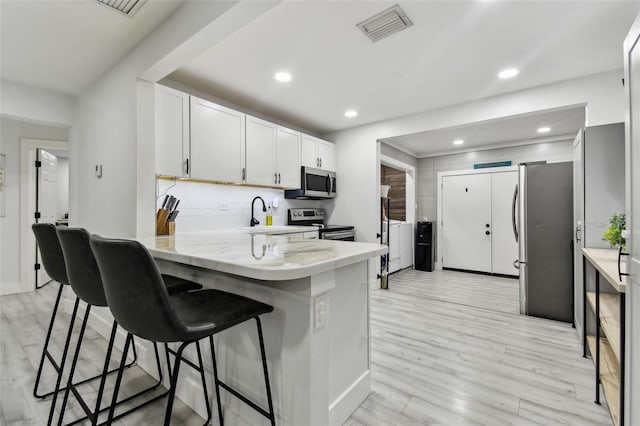 kitchen with white cabinets, light hardwood / wood-style floors, kitchen peninsula, and appliances with stainless steel finishes