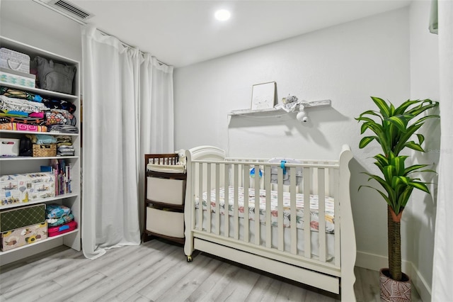 bedroom with a crib, a baseboard heating unit, and light hardwood / wood-style flooring