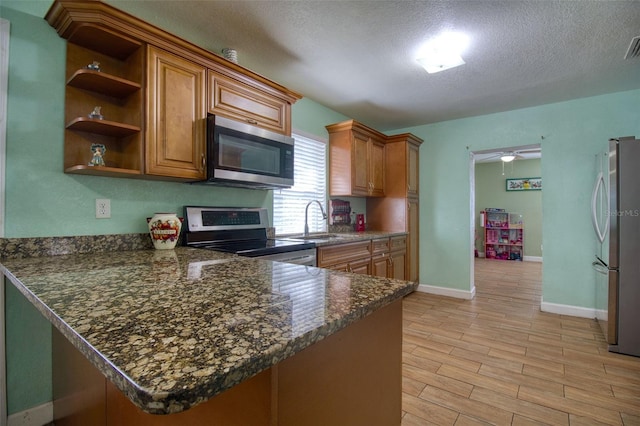 kitchen with a textured ceiling, appliances with stainless steel finishes, light hardwood / wood-style floors, kitchen peninsula, and sink