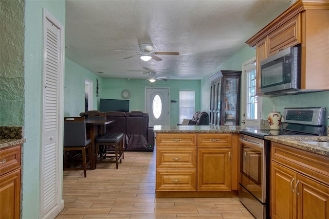 kitchen featuring appliances with stainless steel finishes, light hardwood / wood-style floors, kitchen peninsula, ceiling fan, and a textured ceiling