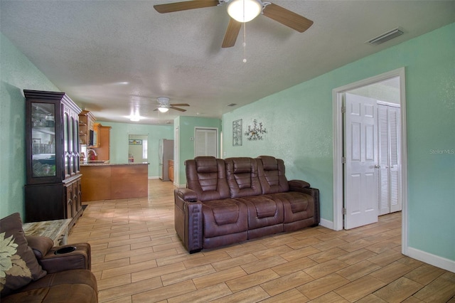 living room with ceiling fan, sink, a textured ceiling, and light hardwood / wood-style flooring