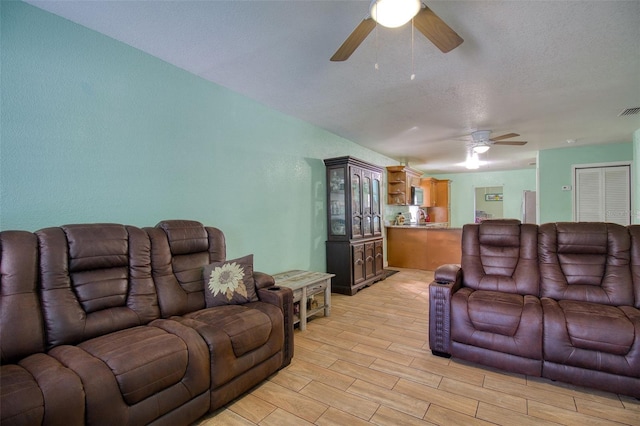 living room featuring a textured ceiling, ceiling fan, and light wood-type flooring