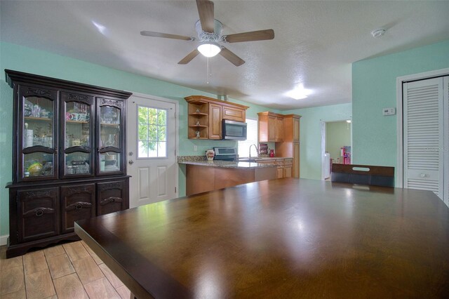 kitchen with a textured ceiling, appliances with stainless steel finishes, kitchen peninsula, sink, and ceiling fan