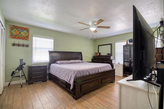 bedroom featuring multiple windows, light hardwood / wood-style flooring, ceiling fan, and a closet