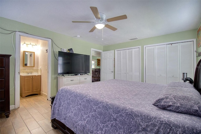 bedroom with a textured ceiling, ensuite bathroom, sink, multiple closets, and ceiling fan