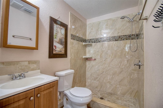 bathroom with tiled shower, vanity, toilet, and a textured ceiling