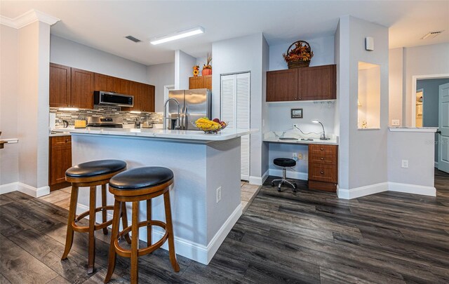 kitchen with a kitchen breakfast bar, dark hardwood / wood-style flooring, a center island with sink, appliances with stainless steel finishes, and tasteful backsplash