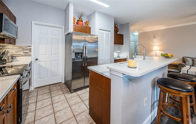 kitchen featuring light tile patterned floors, backsplash, appliances with stainless steel finishes, an island with sink, and a kitchen bar