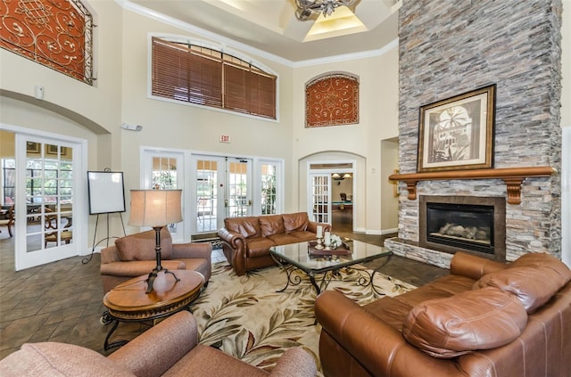 living room featuring a wealth of natural light, a towering ceiling, a stone fireplace, and french doors