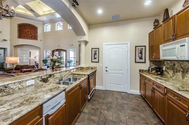 kitchen featuring a towering ceiling, white appliances, light stone counters, and sink