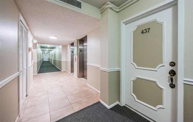 hall with a textured ceiling and light tile patterned floors