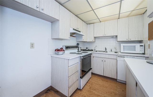 kitchen with light wood-type flooring, white appliances, sink, a drop ceiling, and tasteful backsplash