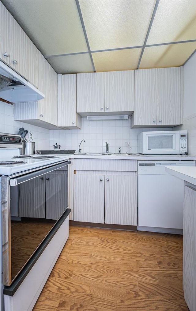 kitchen with a drop ceiling, white appliances, tasteful backsplash, sink, and light hardwood / wood-style floors