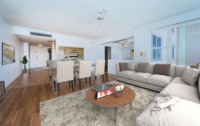 living room with a textured ceiling, ceiling fan, and dark hardwood / wood-style floors