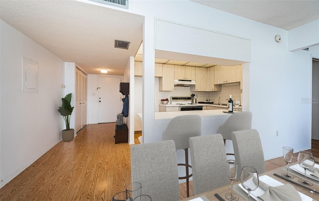 kitchen featuring electric range, light hardwood / wood-style floors, kitchen peninsula, a kitchen bar, and a textured ceiling