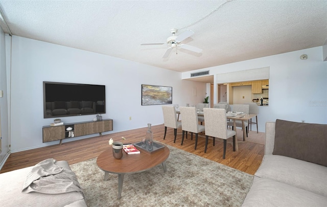 living room with a textured ceiling, wood-type flooring, and ceiling fan