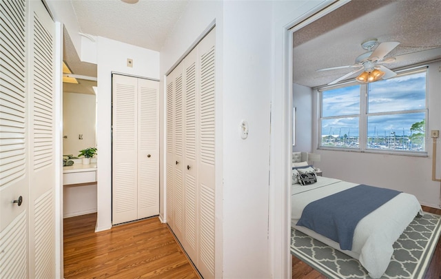 bedroom featuring a textured ceiling, hardwood / wood-style flooring, two closets, and ceiling fan