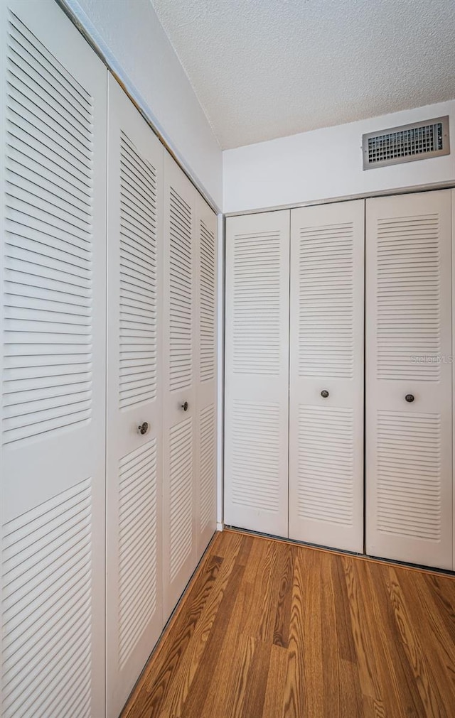 unfurnished bedroom with wood-type flooring, multiple closets, and a textured ceiling