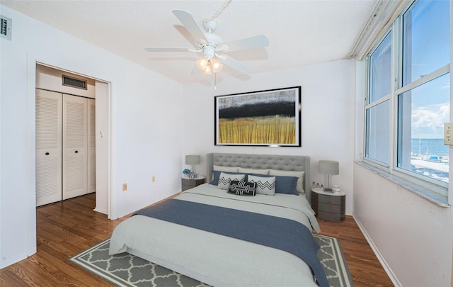 bedroom with dark wood-type flooring, a textured ceiling, ceiling fan, and a closet