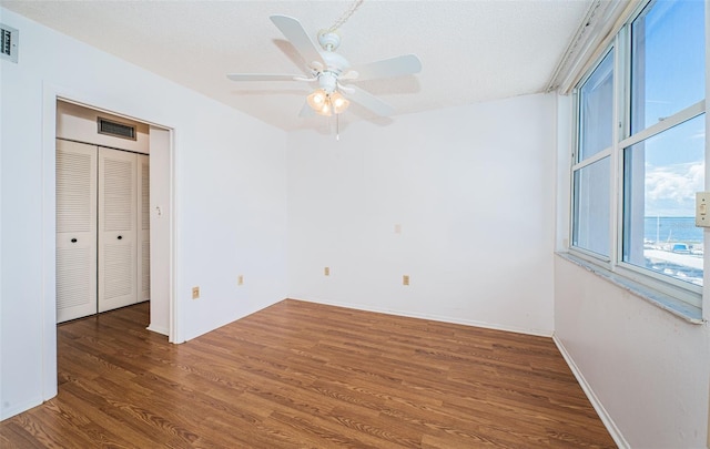 empty room with dark hardwood / wood-style flooring, a water view, ceiling fan, and a textured ceiling