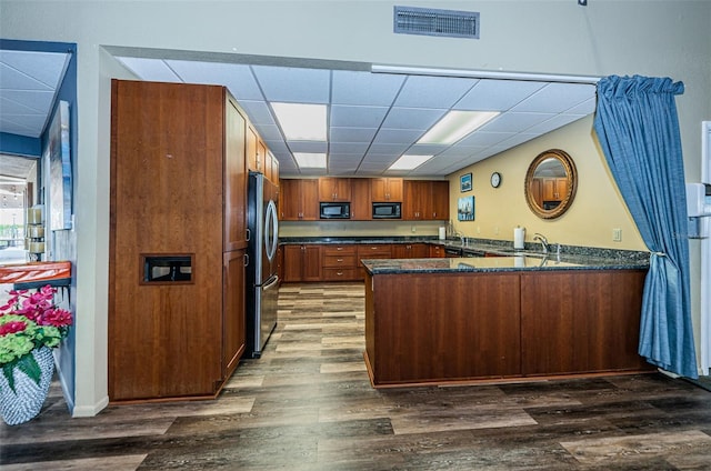 kitchen featuring black microwave, stainless steel refrigerator, dark hardwood / wood-style floors, and kitchen peninsula