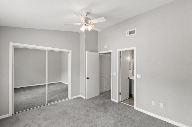 unfurnished bedroom featuring lofted ceiling, ceiling fan, ensuite bathroom, light carpet, and a closet